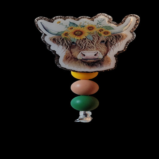 Introducing the Highland Cow Sunflower Badge Reel - adorned with a sunflower headband and playful silicone beads, all complemented by a dark brown glitter background.