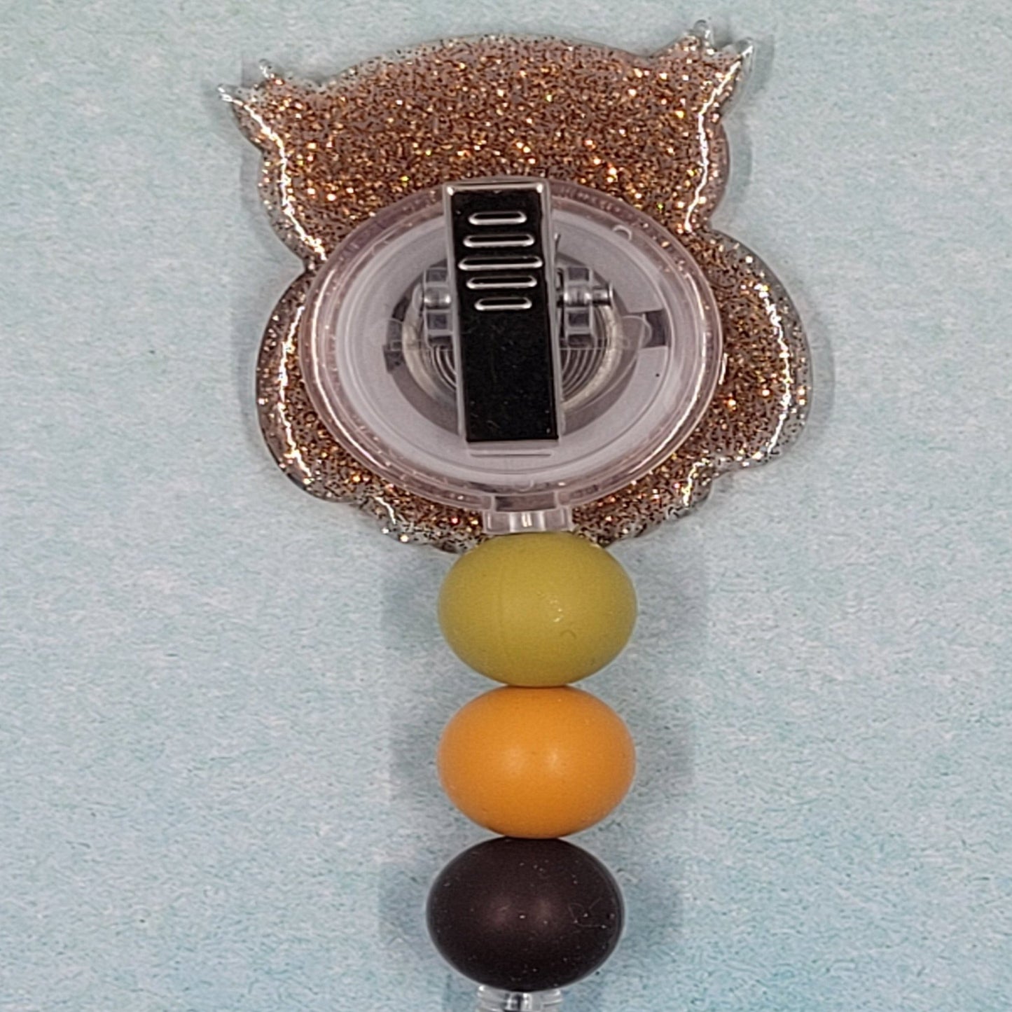 This Badge Reel features a Wise Owl design paired with a shiny brown glitter background. The adorable owl is complemented by three color-coordinated silicone beads for an extra touch of charm. Sure to be a hit with any animal lover.
