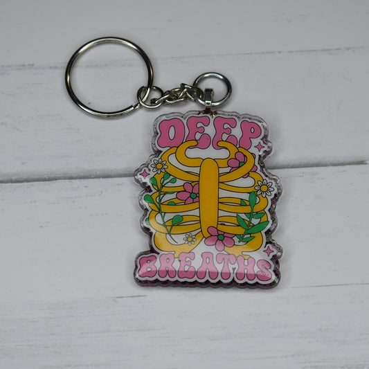 Feeling overwhelmed? Take a moment to relax and just breathe. The Keychain Deep Breaths serves as a helpful reminder to pause, take a deep breath, and refocus. With its sturdy acrylic resin material, it boasts a stylish purple glitter backing and a motivational Deep Breaths design on the front.