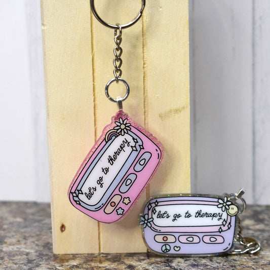 Keychain Lets Go To Therapy is crafted from durable acrylic resin and comes in pink or purple. Perfect for those in need of some therapy on the go.