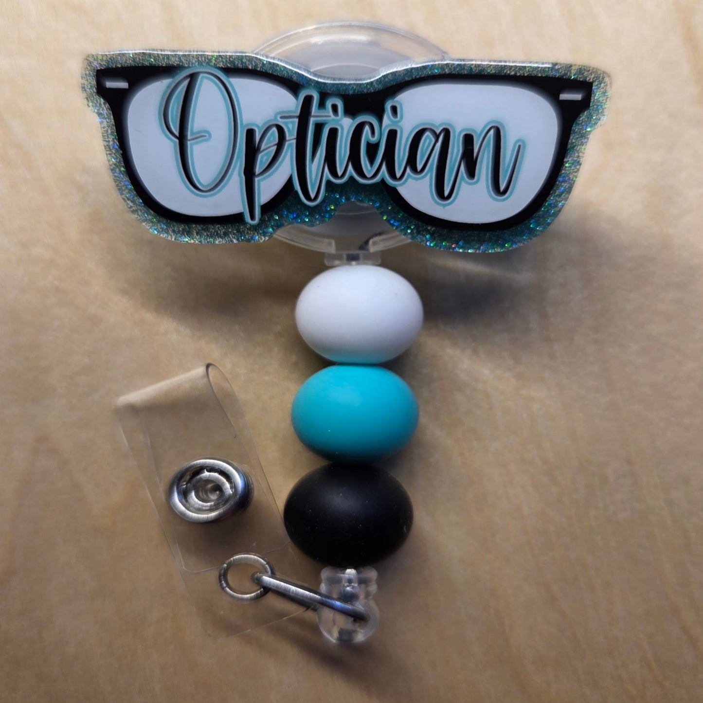 Retractable badge holder with 'Optician' design on a beige background