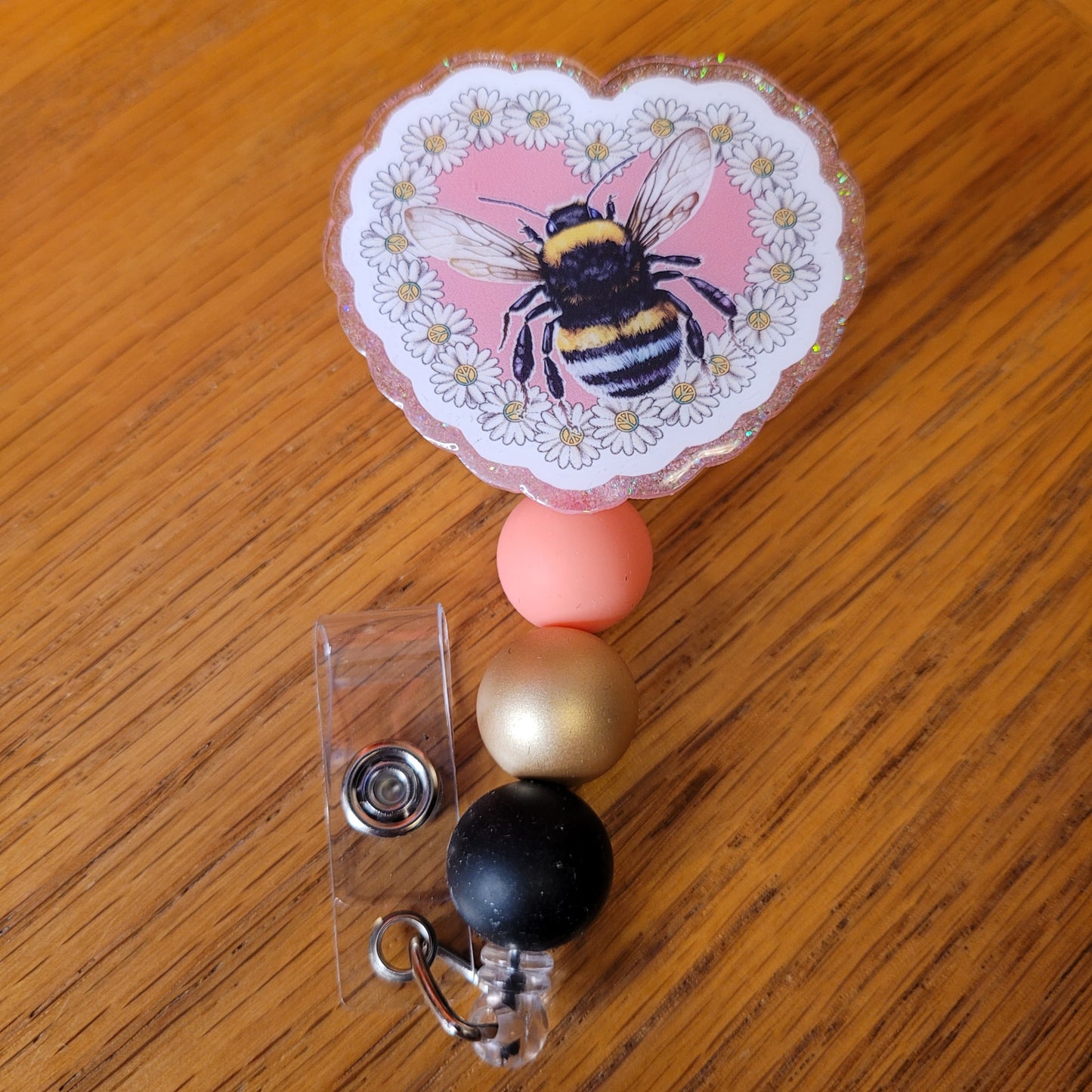 Another new one to our Animal Series... Bee Heart. This badge reel features a heart shaped base with a honey bee centered in a border full of daisies. A dazzling pink glitter backing and 3 color-coordinated silicone beads add the perfect finishing touch to this badge reel.
