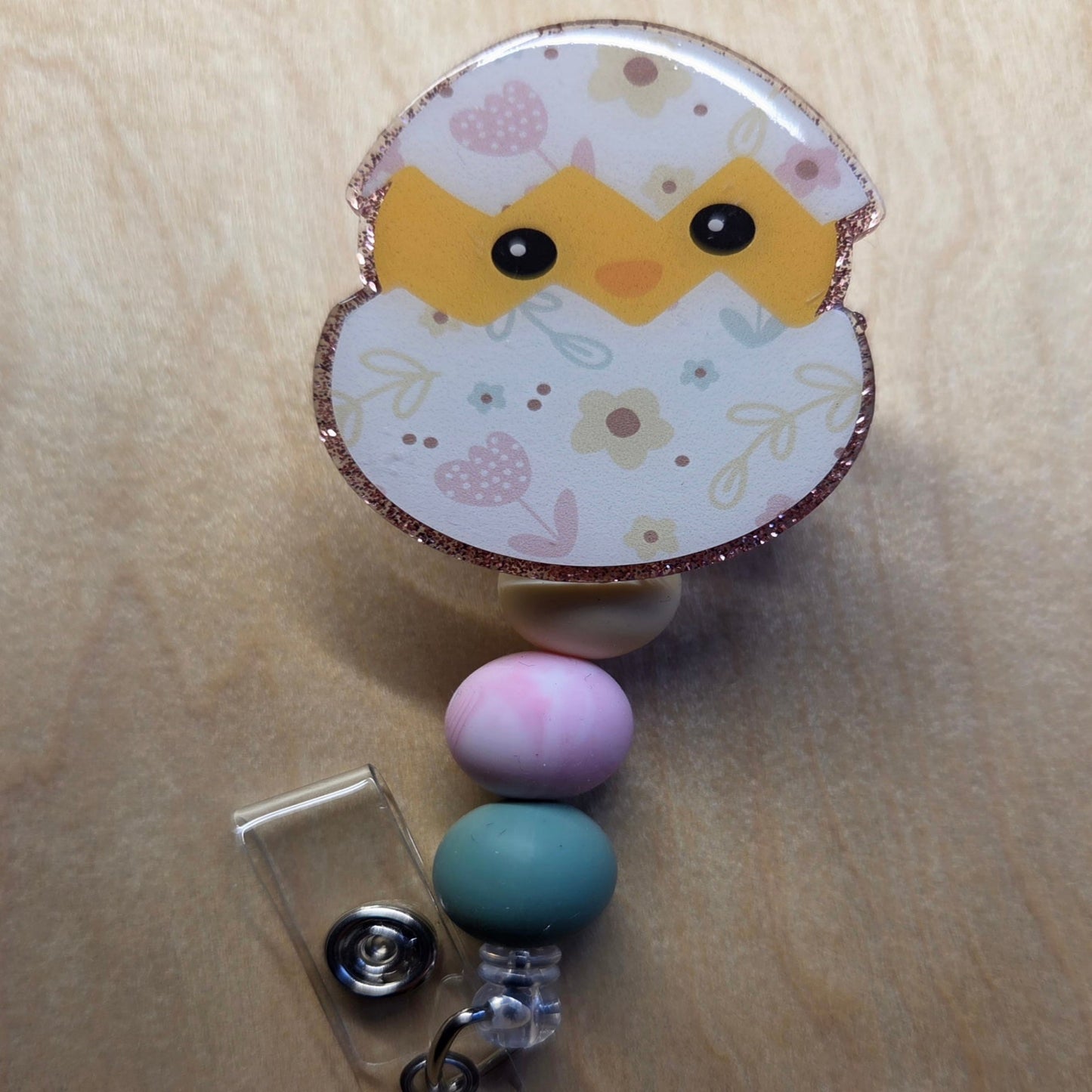 Retractable badge holder with chick design on a wooden surface