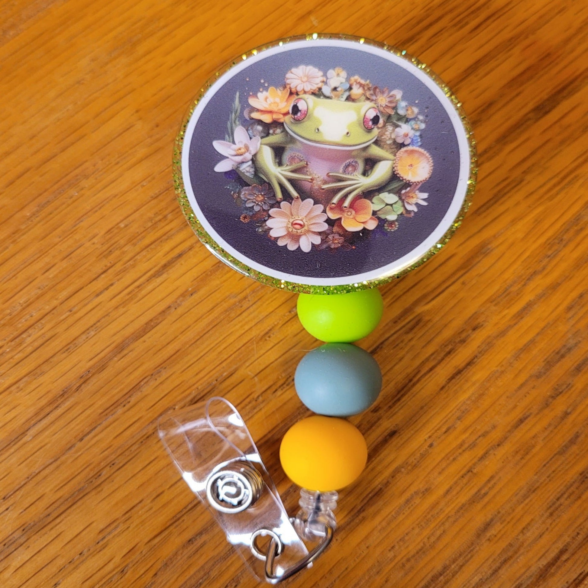 Another new one to our Animal Series... Portrait Of A Frog. This badge reel features a round design with a smiling from posing in a ring of flowers for a special photo op.