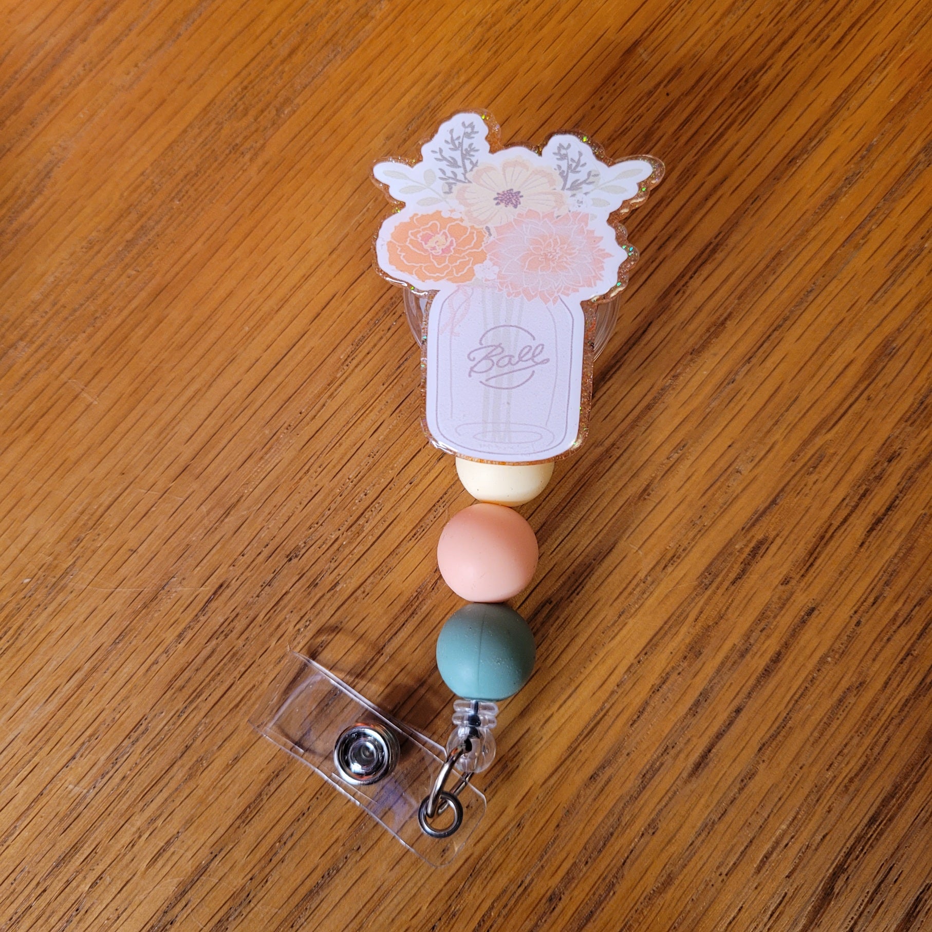 Our Mason Jar Vase badge reel is here. With various flowers in a mason jar used as a vase. A sparkling peach glitter back and embellished with 3 silicone beads on the cord.