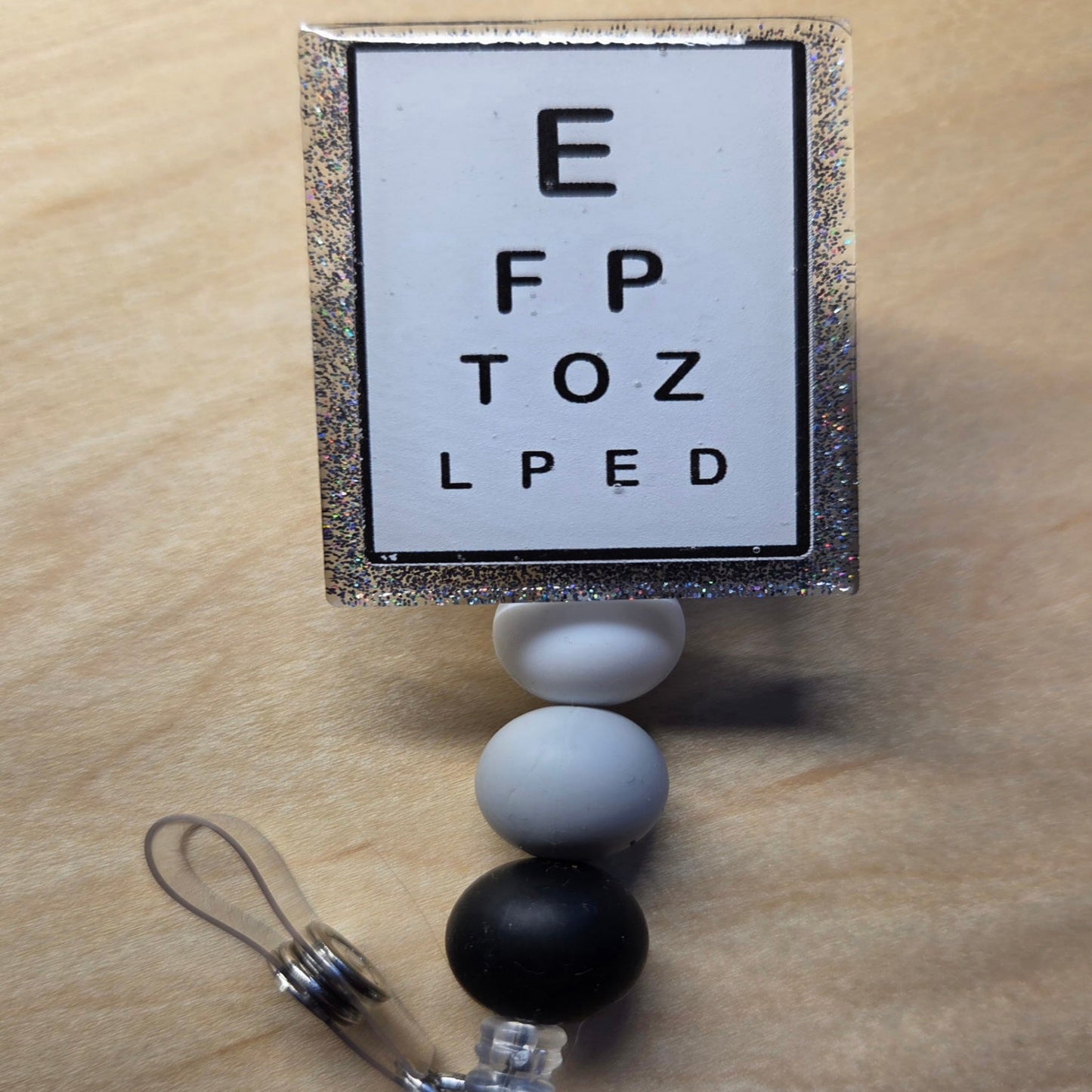 Retractable badge holder with eye chart design on a wooden surface