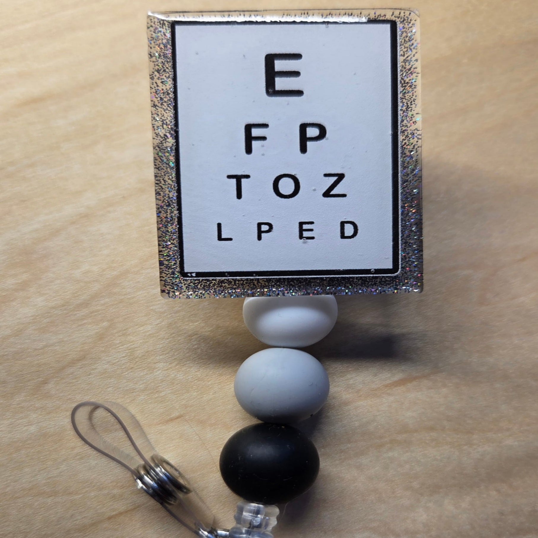 Retractable badge holder with eye chart design on a wooden surface