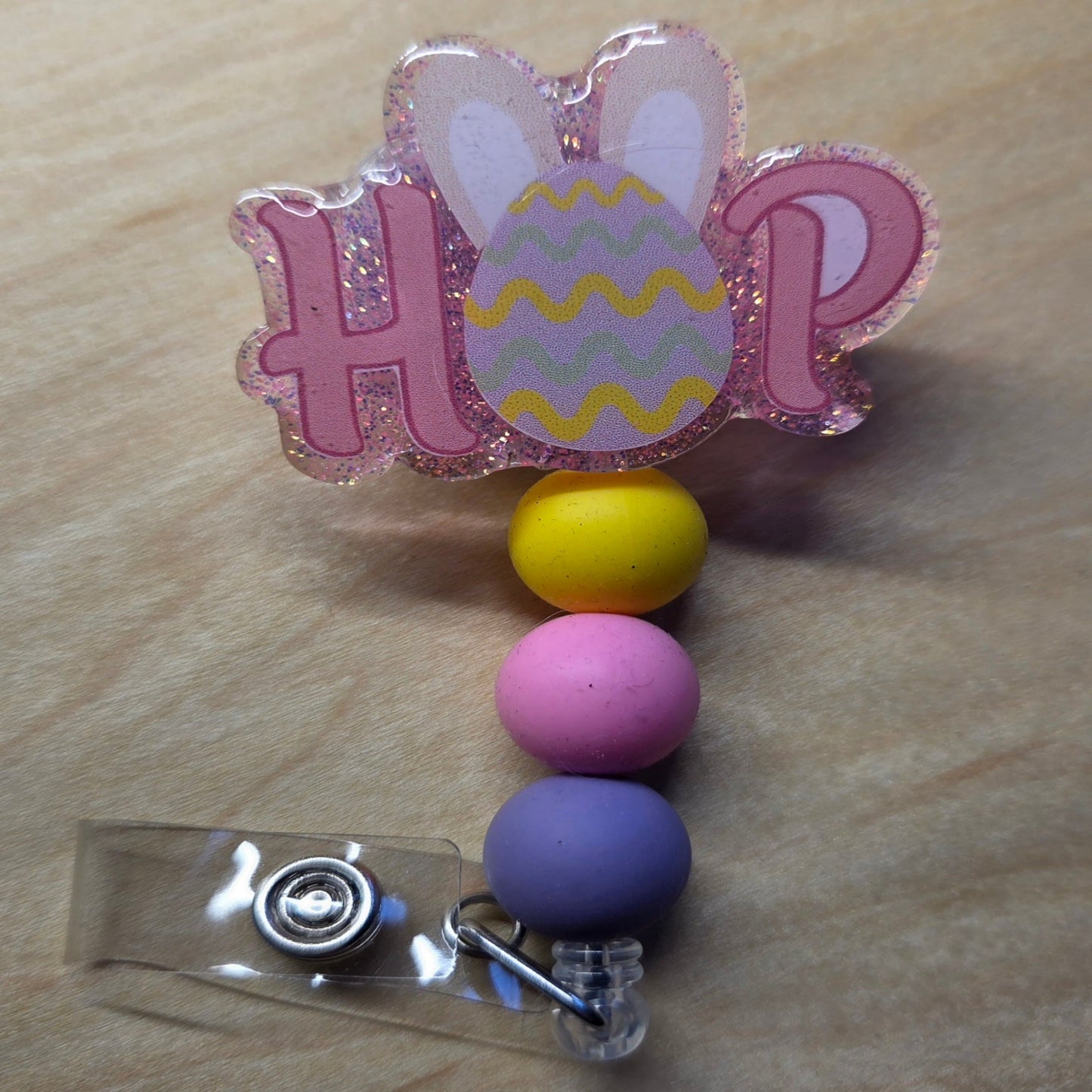 Colorful Easter-themed badge holder with 'HOP' and bunny design on a wooden surface