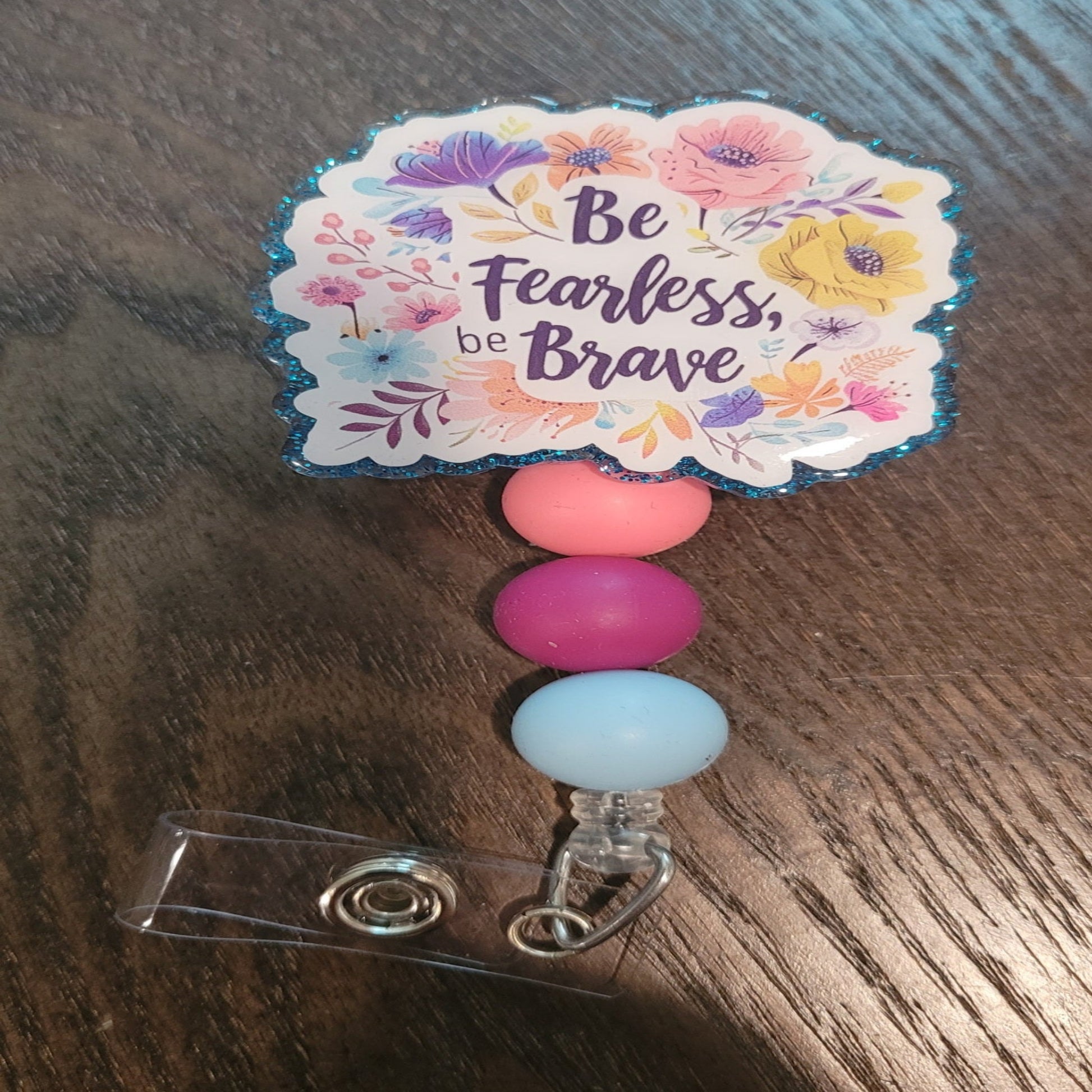 Be Fearless Be Brave is our newest inspirational badge reel. Those words are centered on the front and surrounded by various flowers. Decked With a sparkling blue glitter back and embellished with 3 silicone beads on the cord.