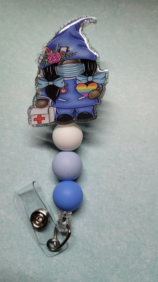 Gnome Nurse at your service. Dressed in blue scrubs with blue ribbons in her hair and carrying a medical kit, she is ready to help any of those in need. Decked out in a sparkling silver glitter back and embellished with 3 silicone beads.