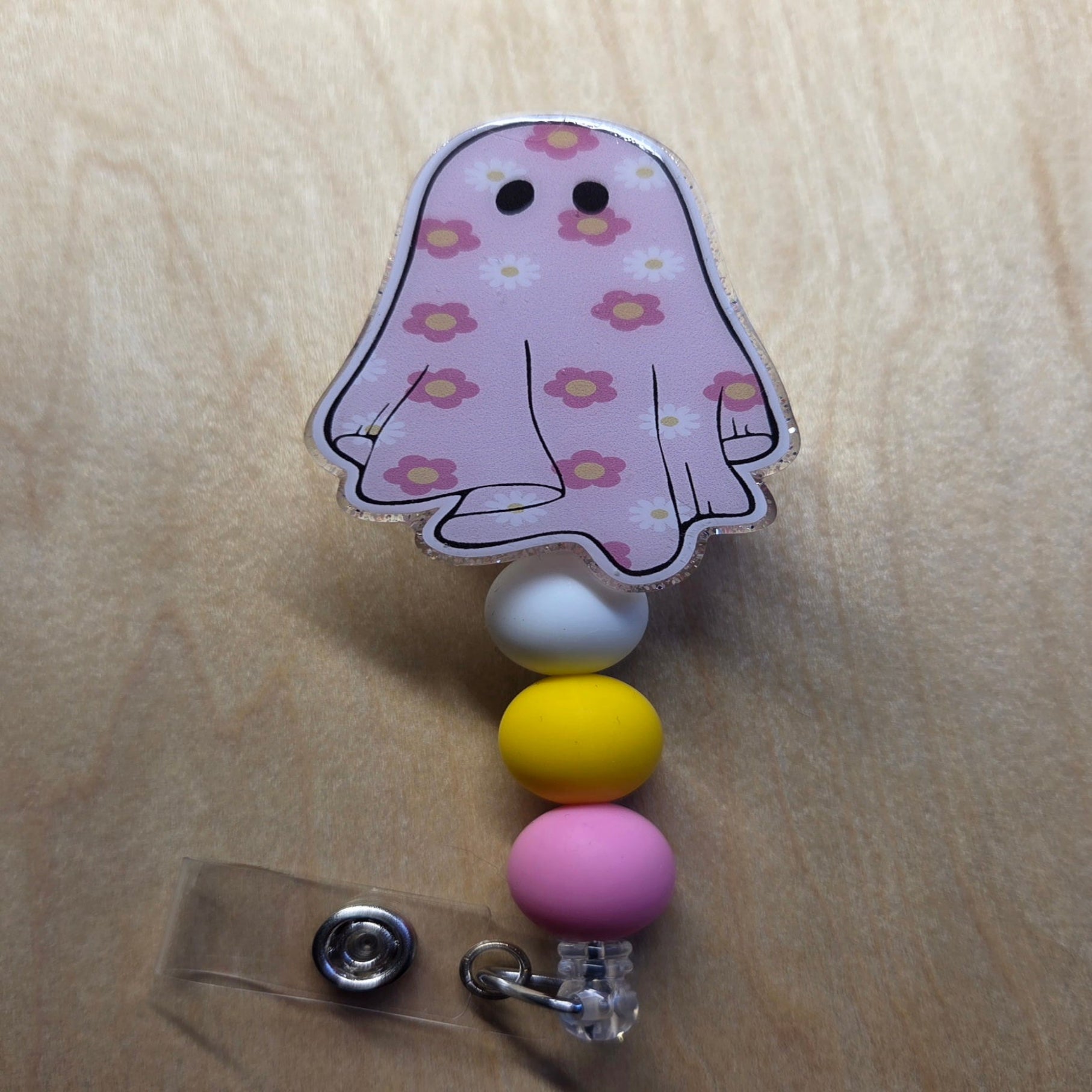 Ghost-shaped badge holder with colorful beads on a wooden surface