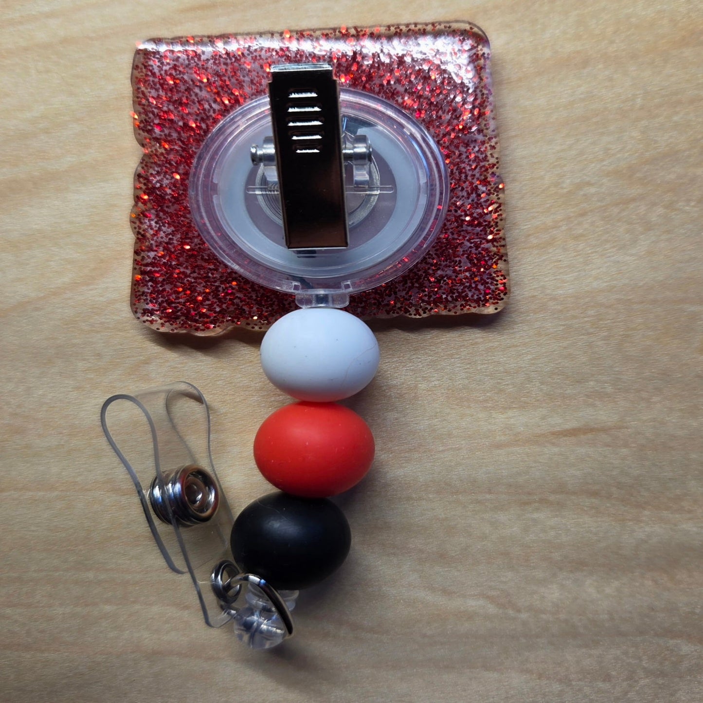 Retractable badge holder with colorful beads and a glittery case on a wooden surface