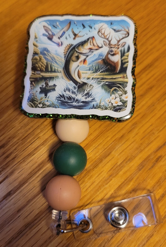 Here is Outdoors. This badge reel has everything from a largemouth bass, dream whitetail buck and flocks of mallards with an image of a person in a boat on a quite lake deep in the woods with a mountain range in the backdrop. It is finished with a green glitter base and three carefully chosen silicone beads.
