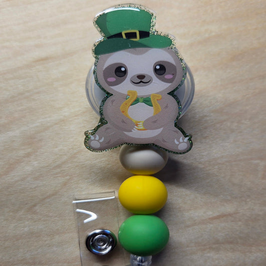 Retractable badge holder with a sloth design wearing a green hat on a wooden surface
