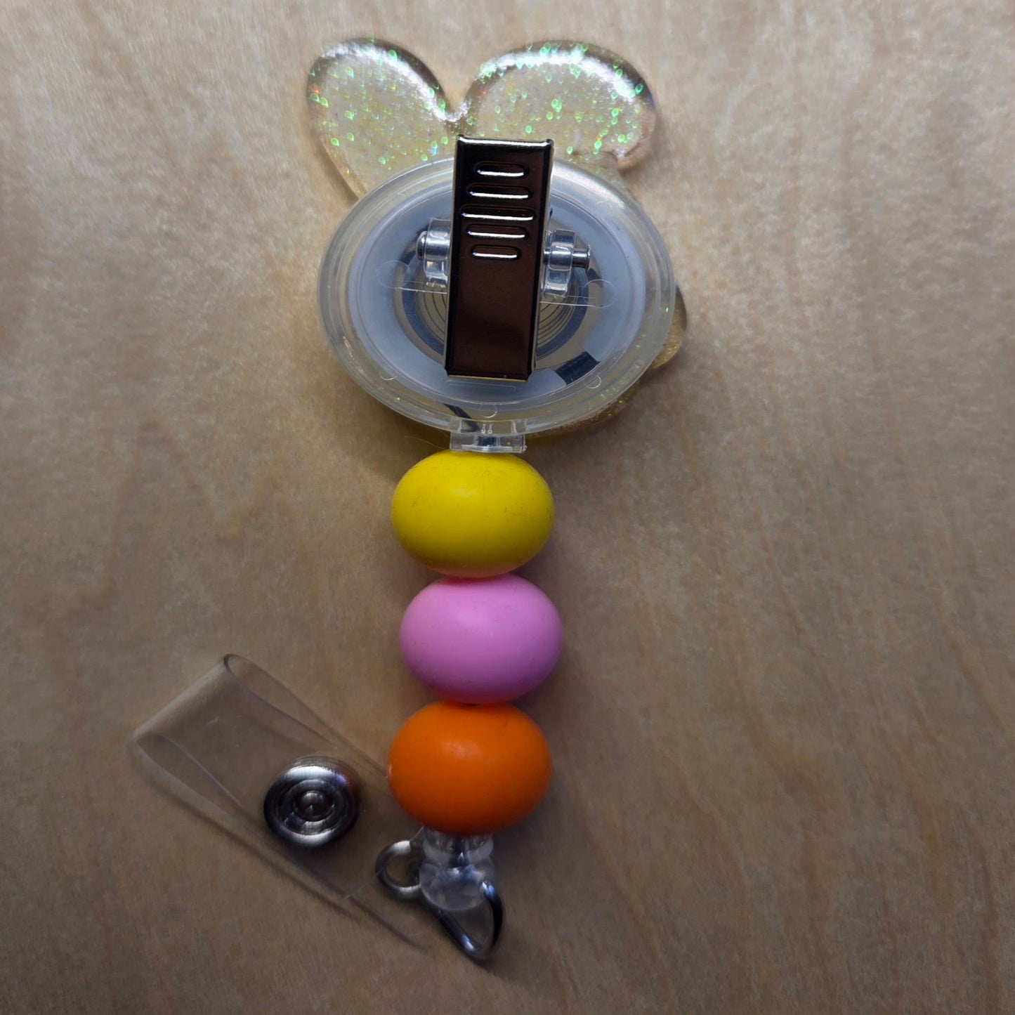 Retractable badge holder with colorful beads and a clear clip on a wooden surface