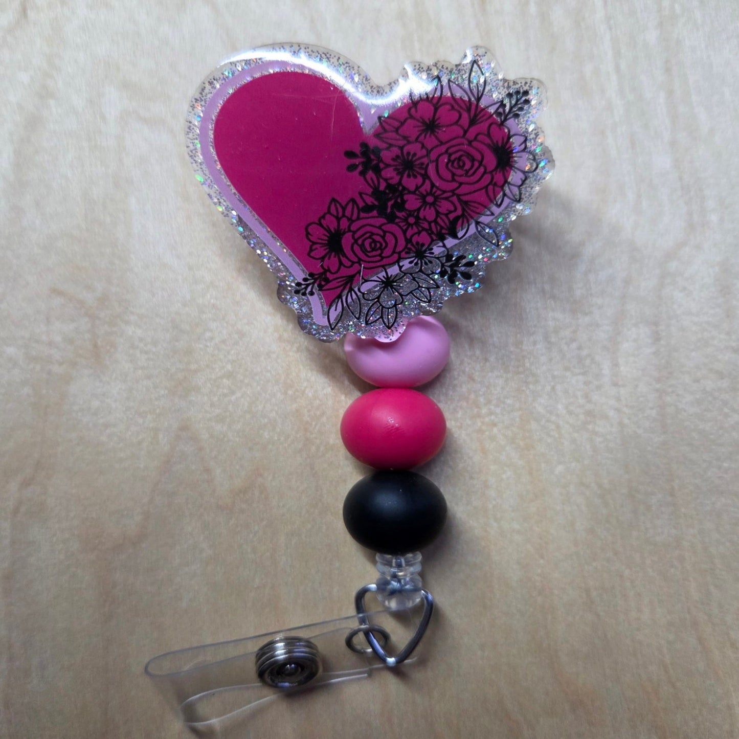 Heart-shaped badge holder with pink, black, and purple beads on a wooden surface