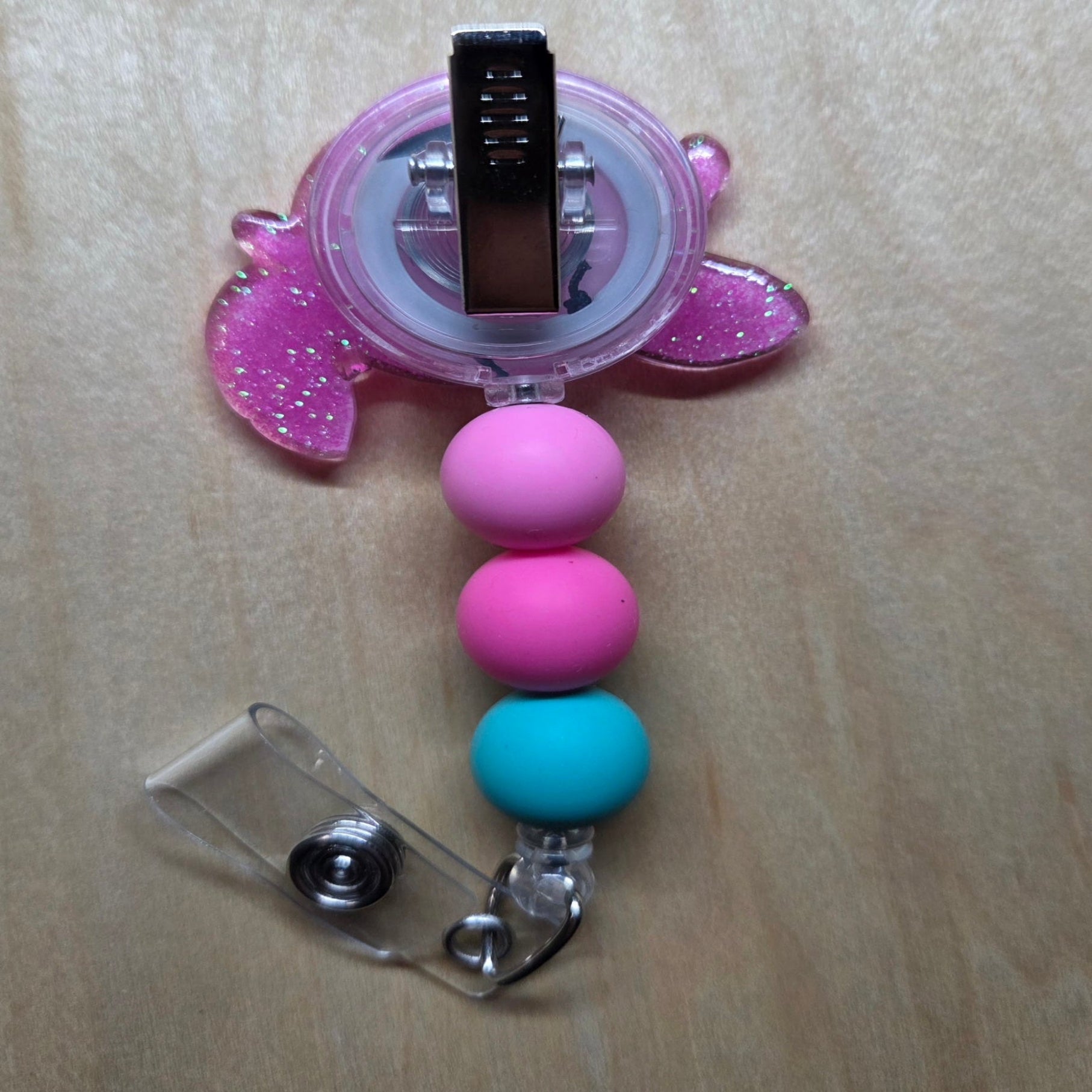 Pink and blue beaded badge holder with a clip on a light wooden surface