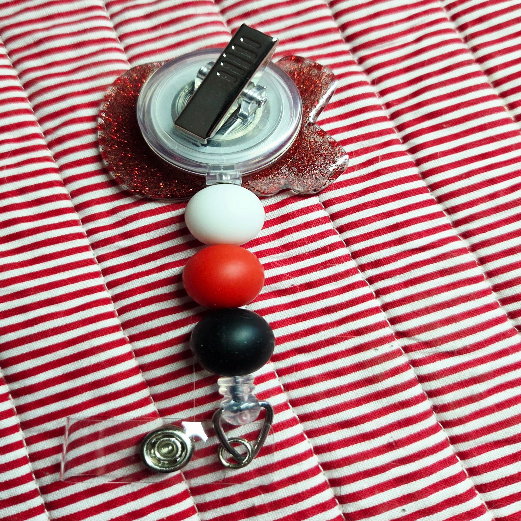 Retractable badge holder with colorful beads on a red and white striped fabric background