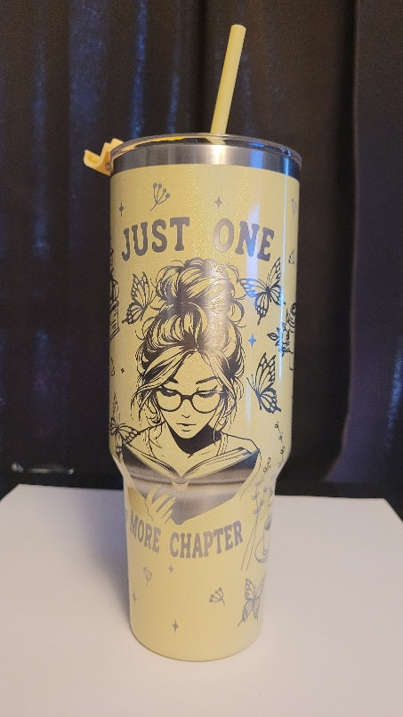Tumbler with a design of a woman reading a book and text 'Just One More Chapter' on a dark background.