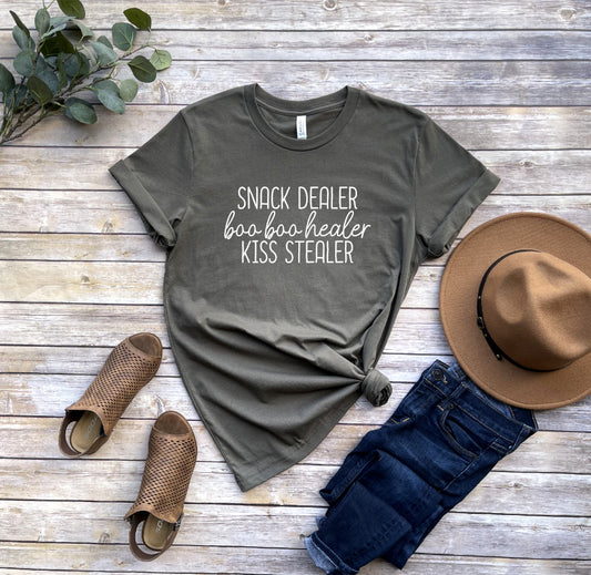 Featuring a white screen printed transfer, the Ultimate Parent T-Shirt Snack Dealer Boo Boo Healer Kiss Stealer is a unisex top crafted from 5.3 oz. of preshrunk 100% cotton.